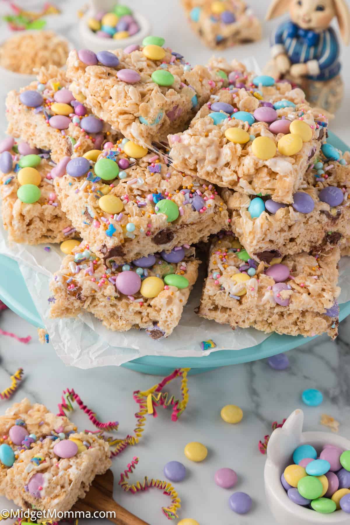 A stack of rice cereal treats decorated with colorful sprinkles and candy on a blue plate, suggesting a festive occasion.