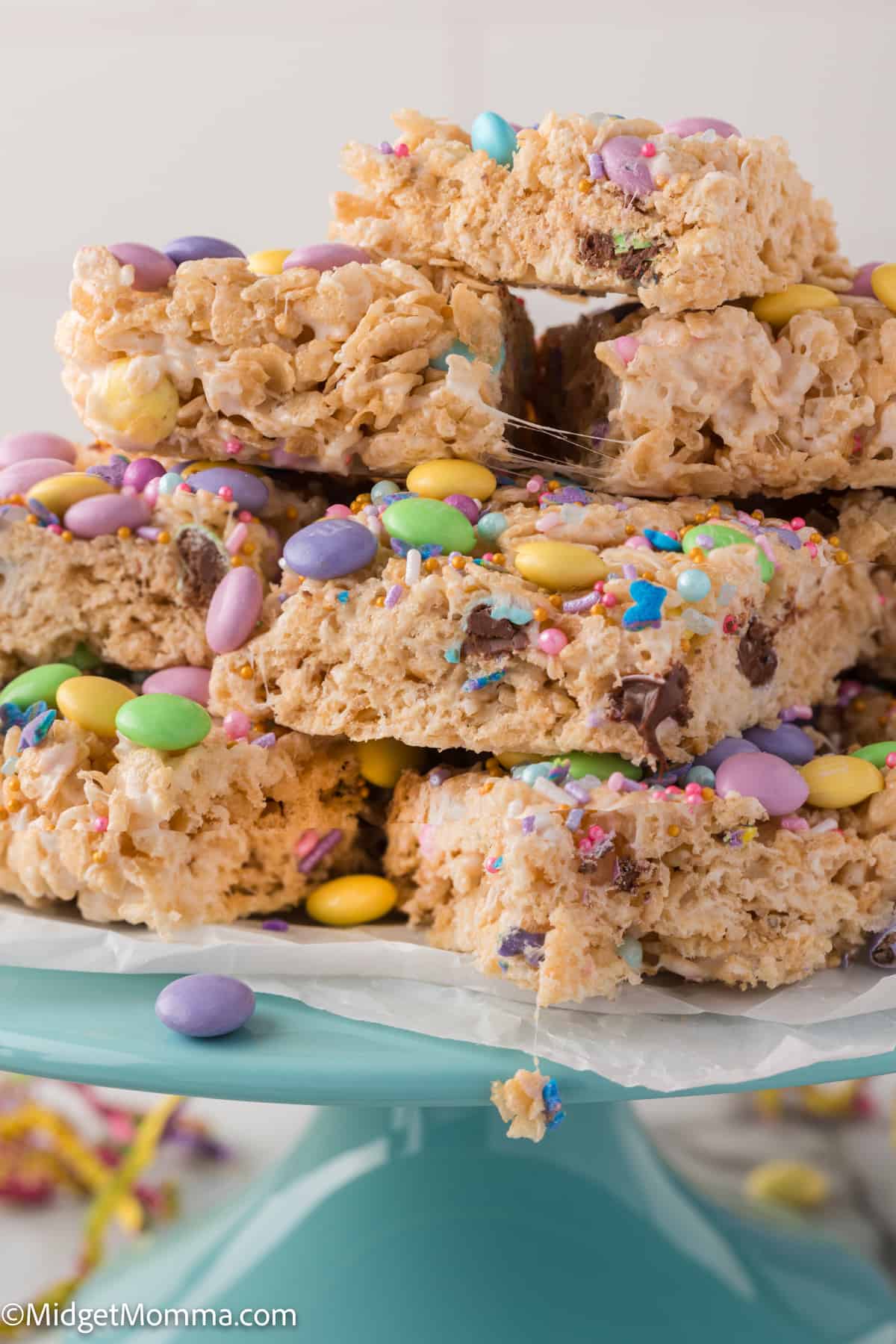 A stack of colorful rice krispie treats with sprinkles and candy on a blue plate.