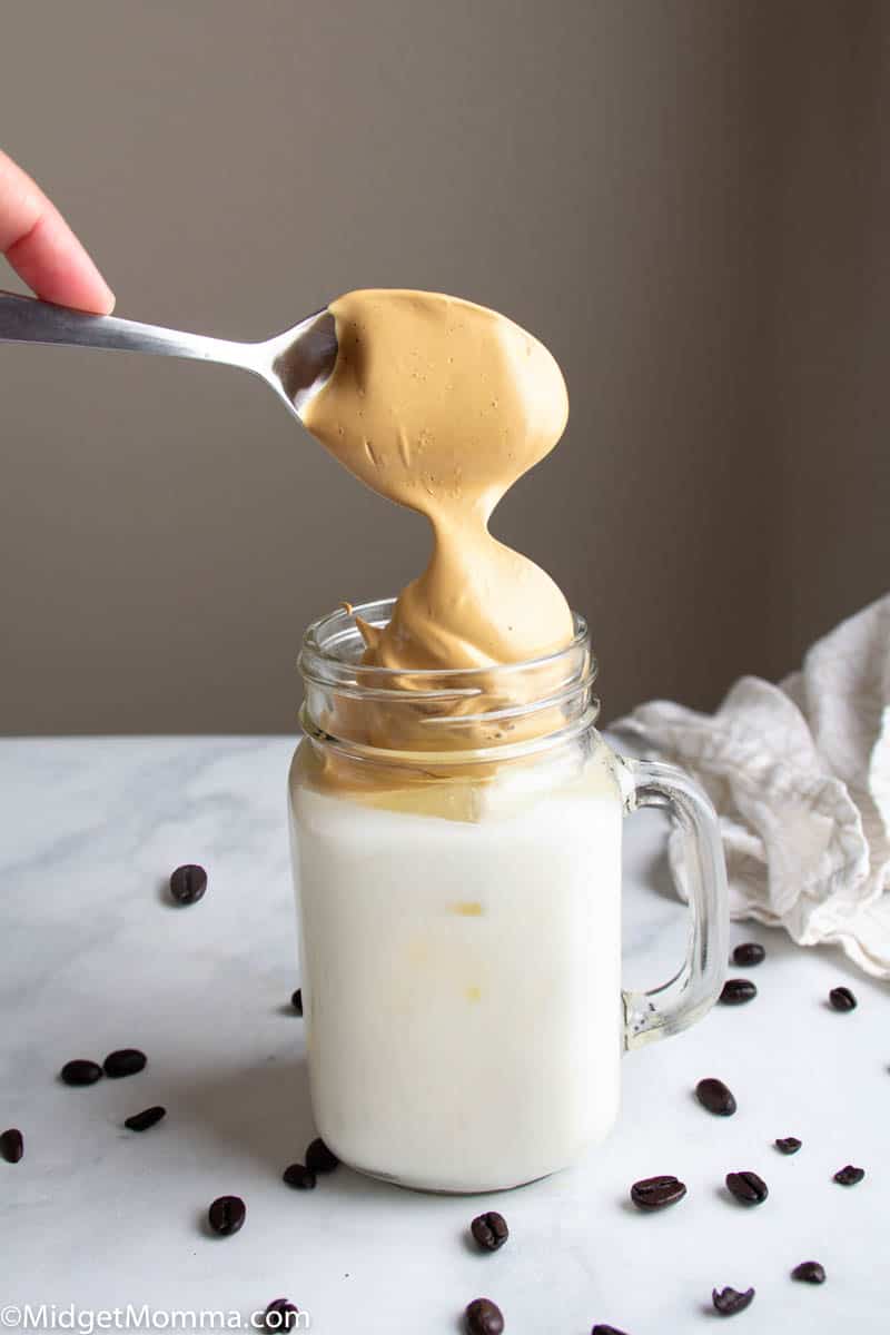 whipped coffee being added to a mason jar glass with milk