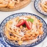 Homemade Funnel Cakes on a plate topped with confectioner's sugar and fresh strawberries