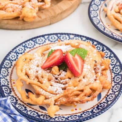 Homemade Funnel Cakes on a plate topped with confectioner's sugar and fresh strawberries