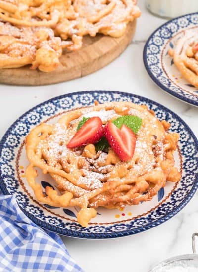 Homemade Funnel Cakes on a plate topped with confectioner's sugar and fresh strawberries