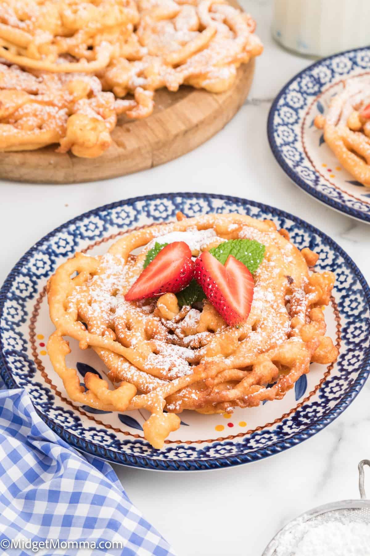 Homemade Funnel Cakes on a plate topped with confectioner's sugar and fresh strawberries