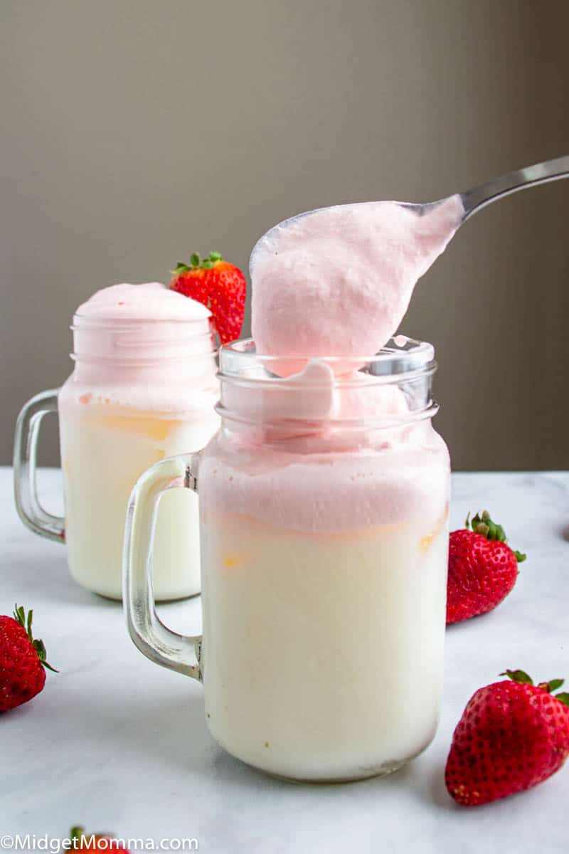 glass of milk with ice being topped with whipped strawberry syrup