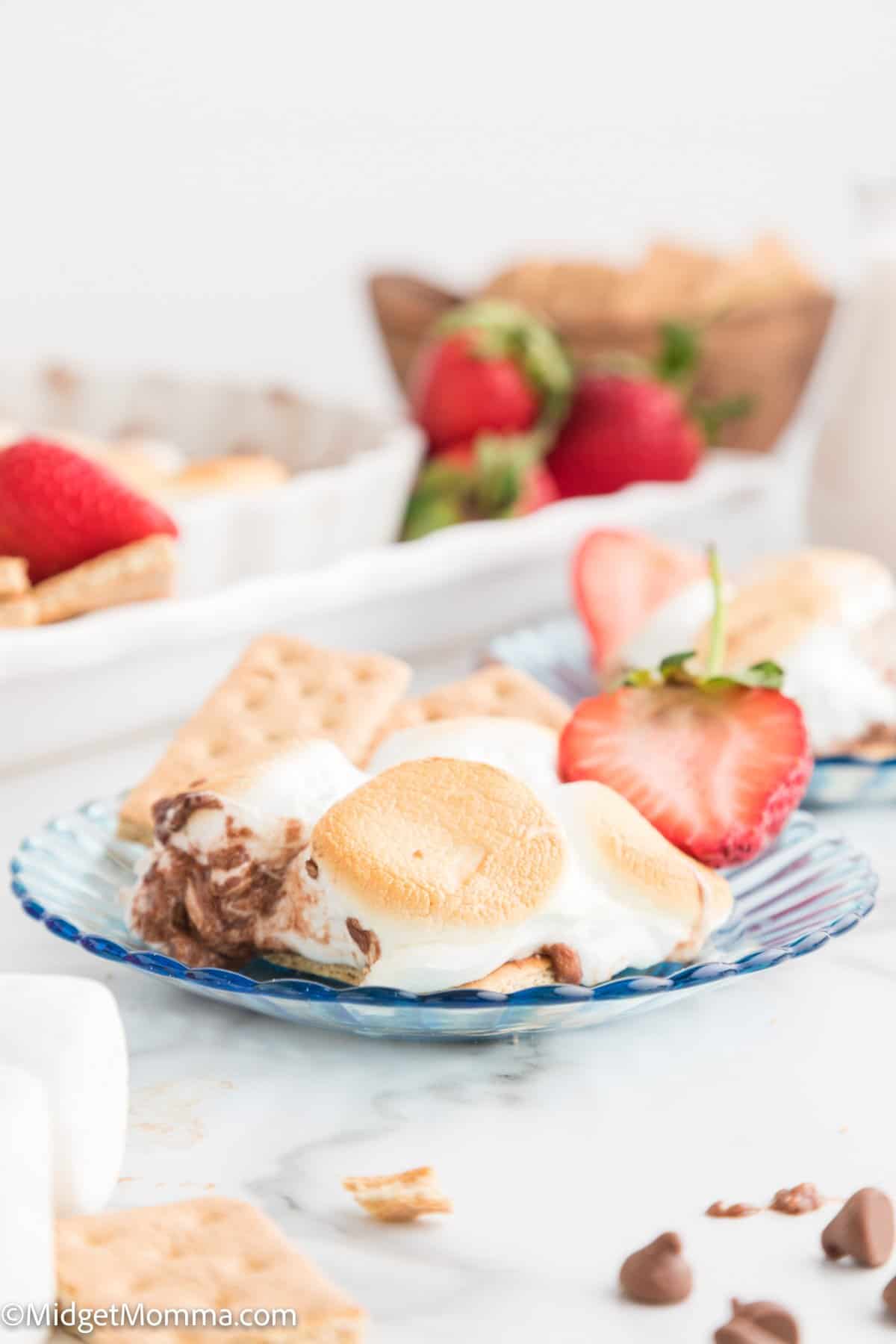 close up photo of Baked S'mores dip on a plate with strawberries and cookies