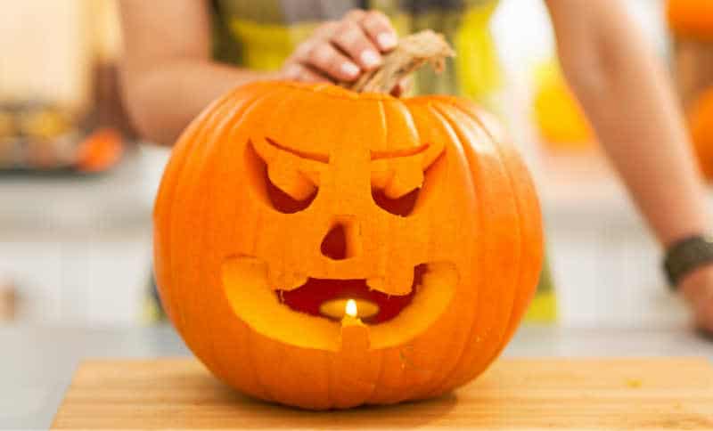 Closeup on big pumpkin Jack-O-Lantern in the Halloween decorated kitchen with candle inside