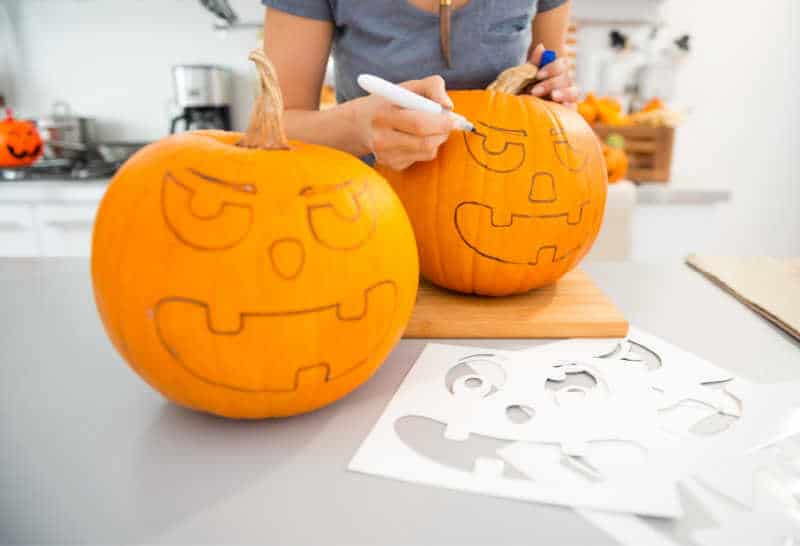 Close up on woman creating pumpkins Jack-O-Lantern for Halloween party in kitchen. Traditional autumn holiday