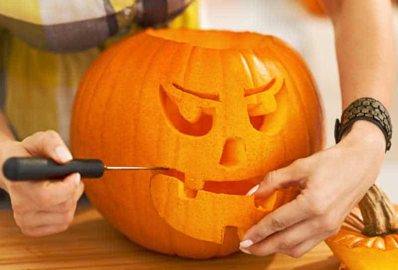 Closeup on person in the Halloween decorated kitchen carving a big orange pumpkin Jack-O-Lantern