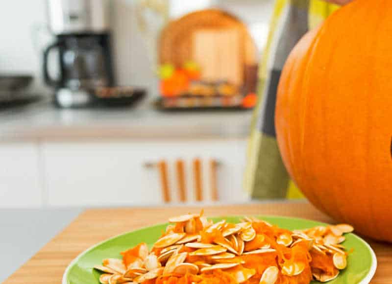 Closeup on young person in the Halloween decorated kitchen prepare big orange pumpkin for carving