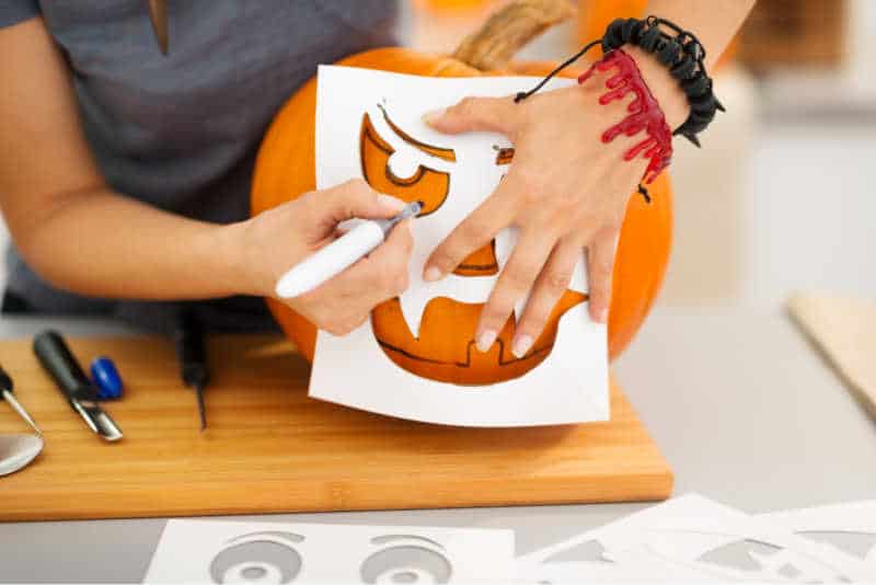 Close up on woman creating pumpkins Jack-O-Lantern for Halloween party in kitchen. Traditional autumn holiday