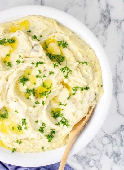 Mashed potatoes in a white bowl with a wooden spoon.