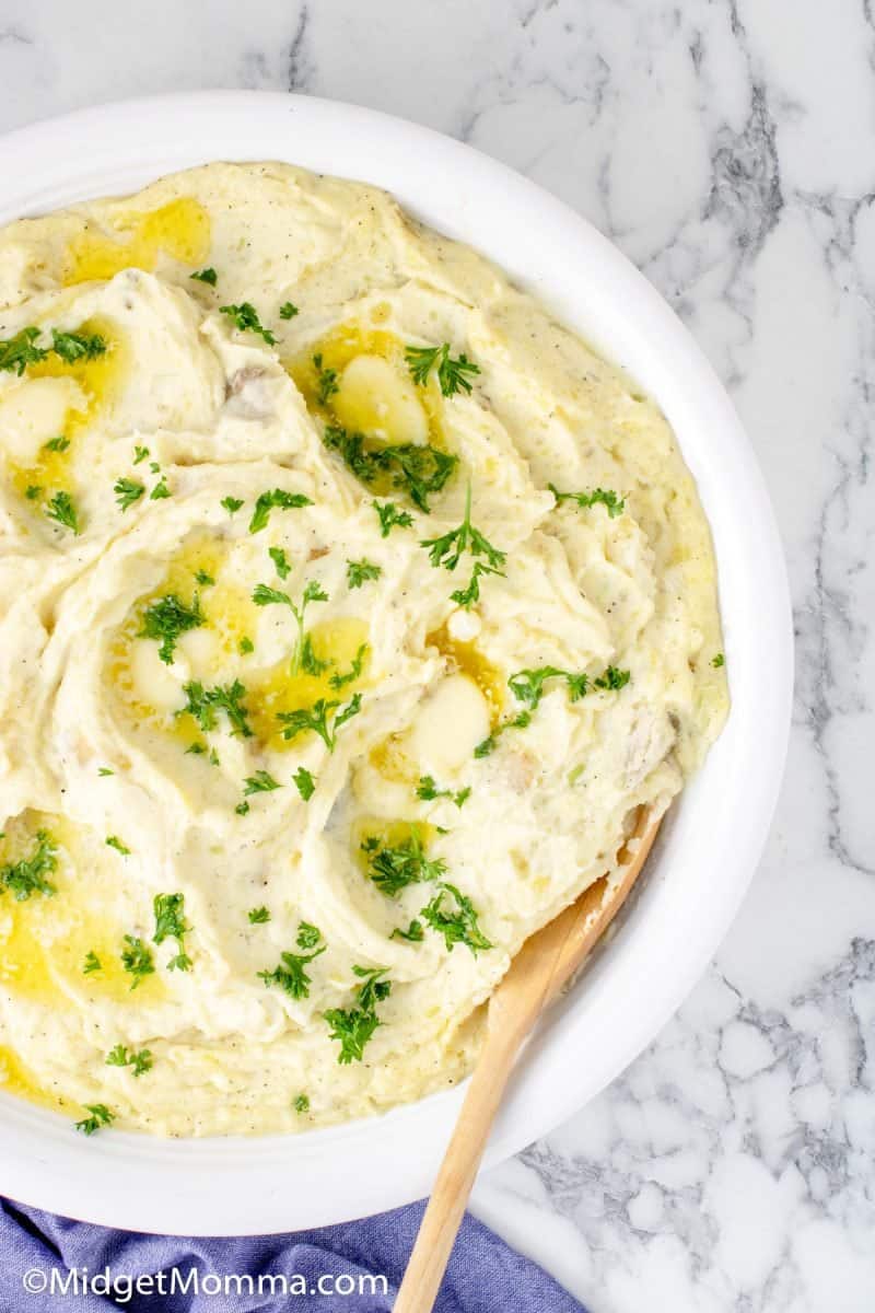 Mashed potatoes in a white bowl with a wooden spoon.