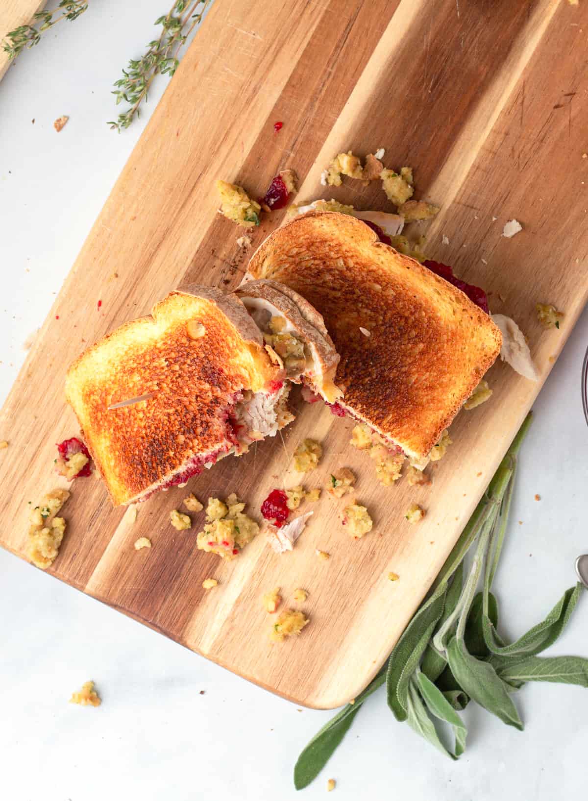 A thanksgiving leftovers turkey sandwich on a cutting board with sprigs of sage.