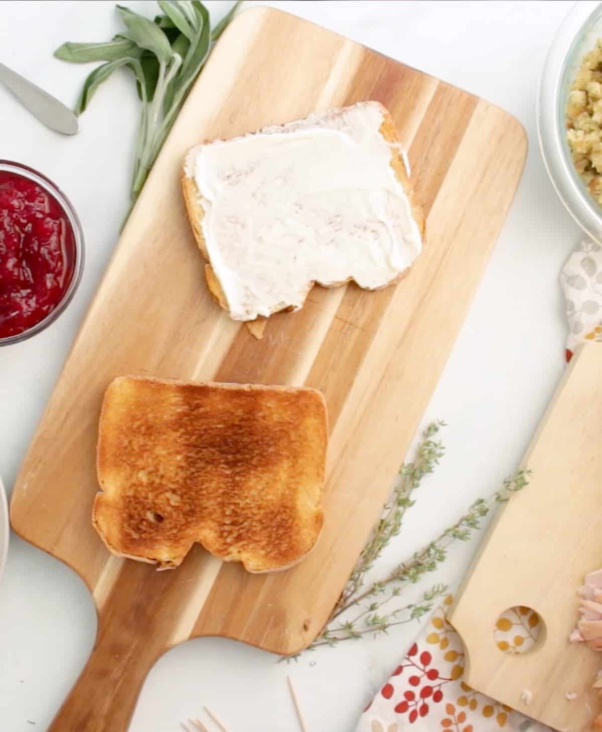 Sliced bread with may on it, slices of turkey and cranberry sauce in bowls next to it.