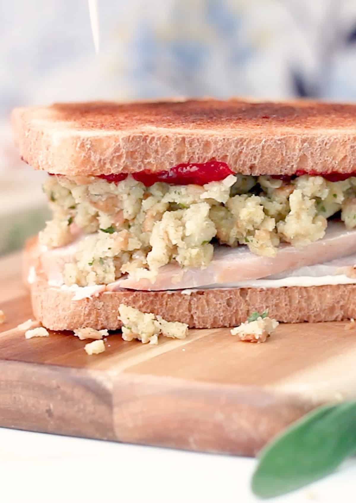 A thanksgiving leftovers turkey sandwich with stuffing on a cutting board.