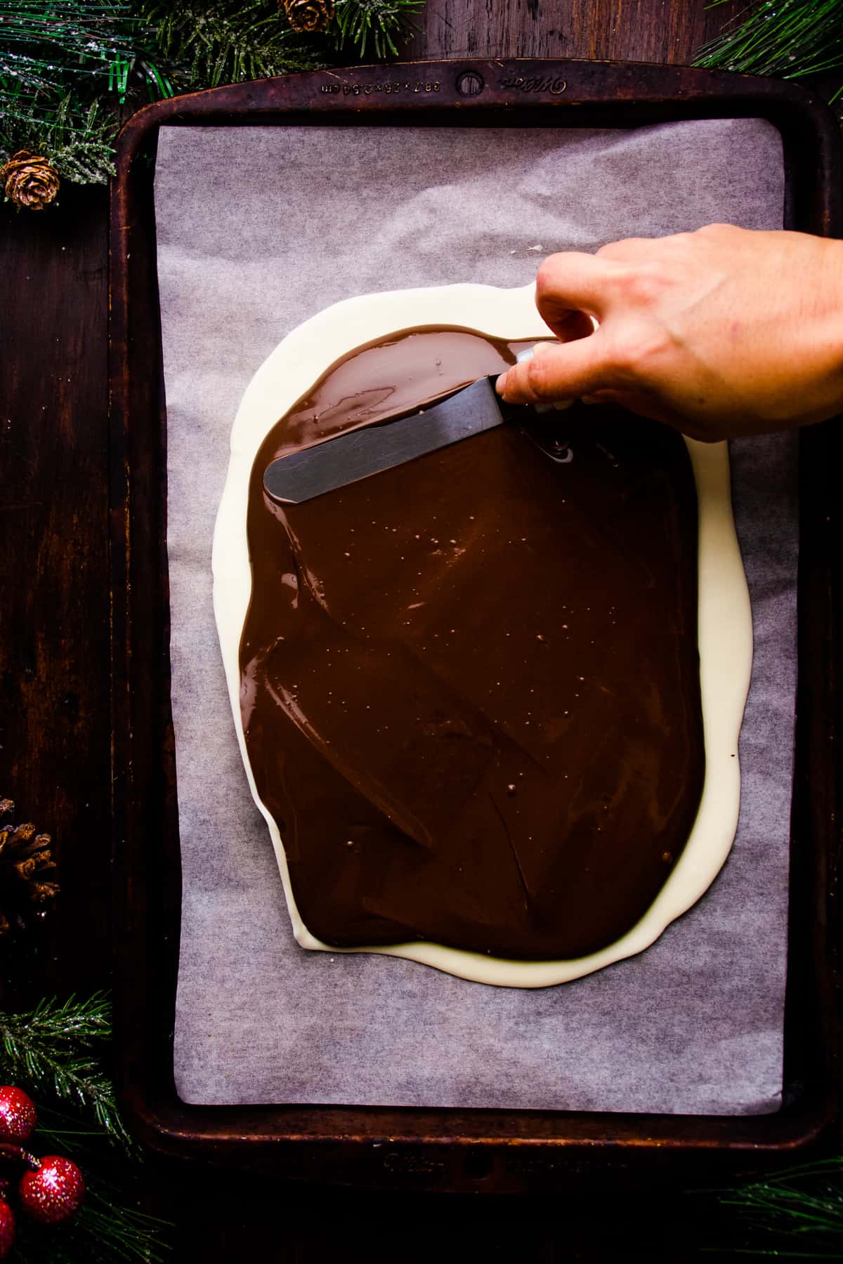 A person is spreading melted chocolate on a baking sheet.