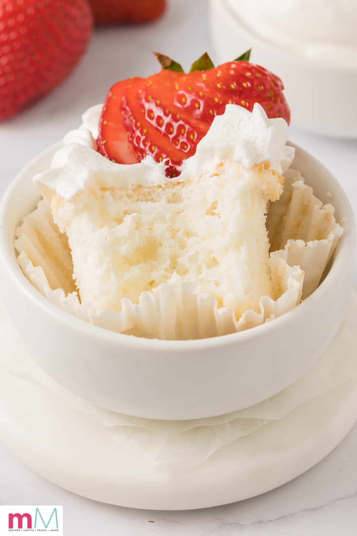 angel food cupcake in a bowl topped with whipped cream and a strawberry