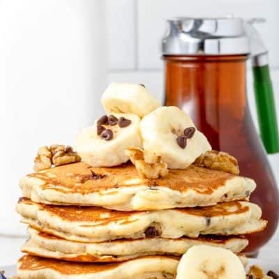front photo of a stack of Chunky Monkey Pancakes on a plate with a bottle of real maple syrup in the background