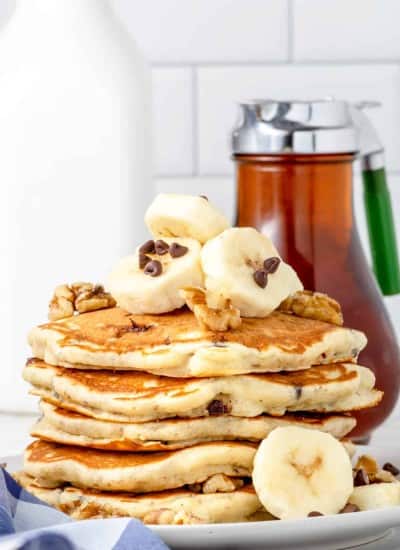 front photo of a stack of Chunky Monkey Pancakes on a plate with a bottle of real maple syrup in the background
