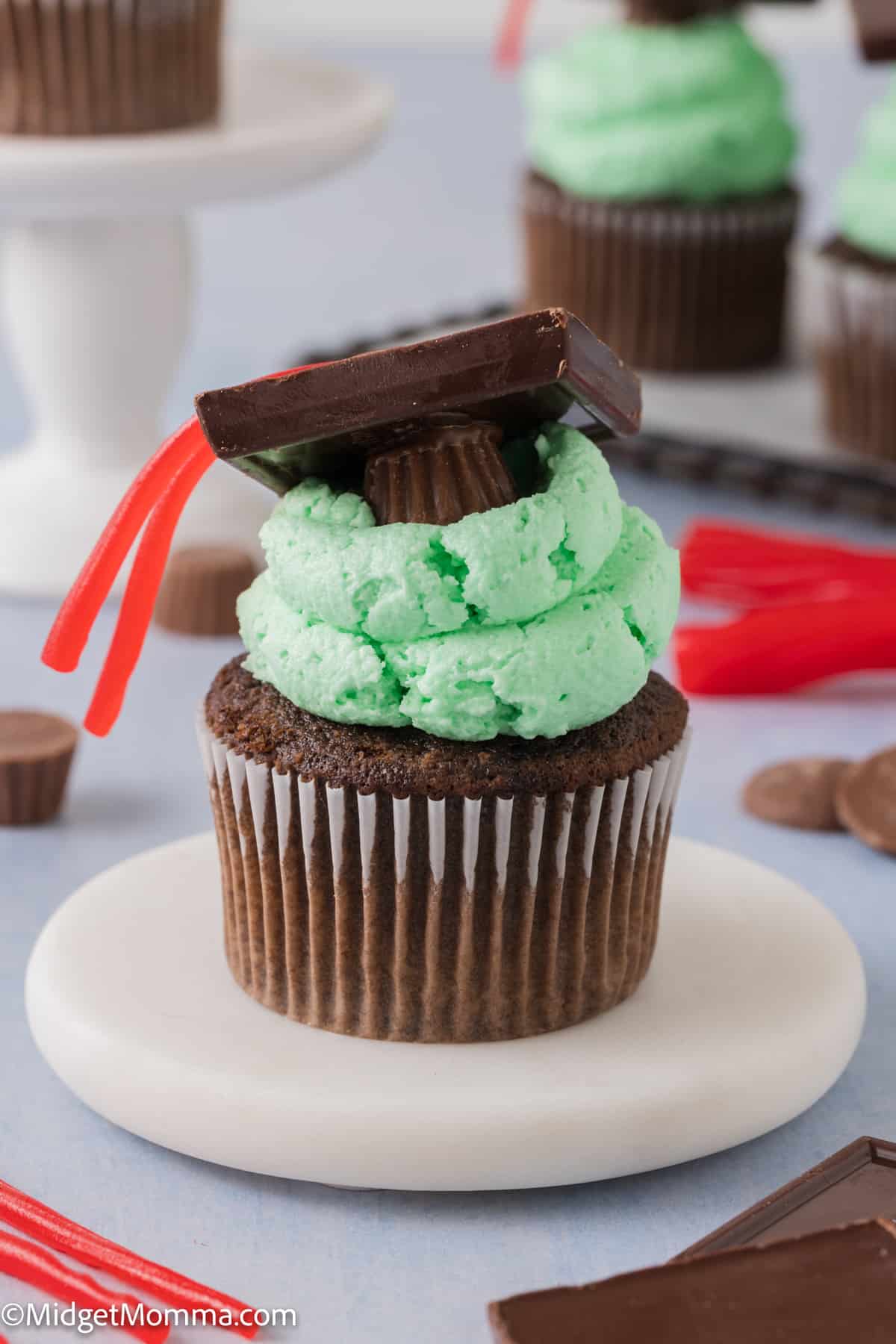 Chocolate cupcakes with green frosting and graduation topper made with peanut butter cups and chocolate squares.
