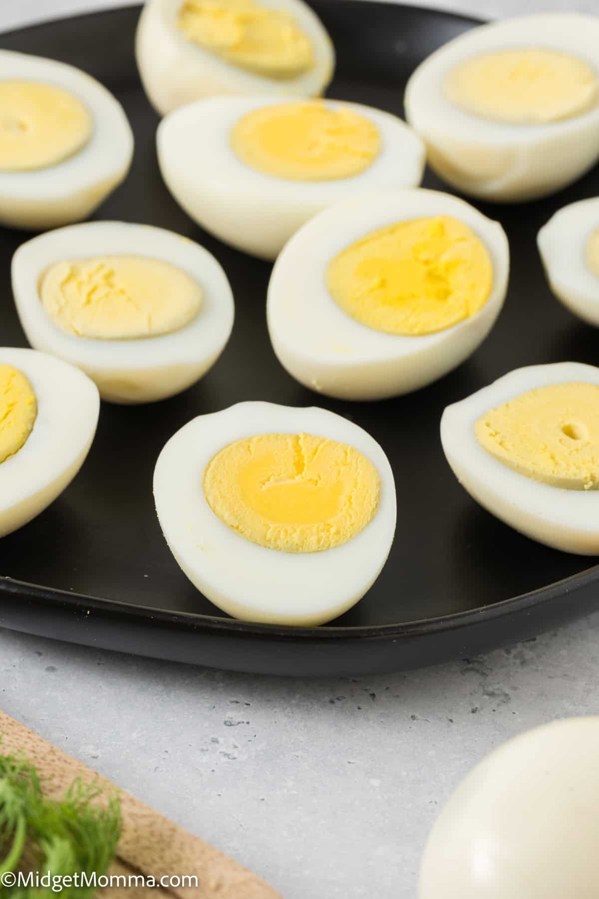 Halved hard-boiled eggs with bright yellow yolks displayed on a black skillet, with a partial view of eggs on a white plate in the foreground.