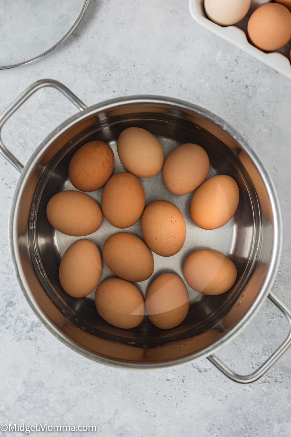 A stainless steel pot containing several brown eggs on a stovetop, viewed from above, with a few eggs on the side.