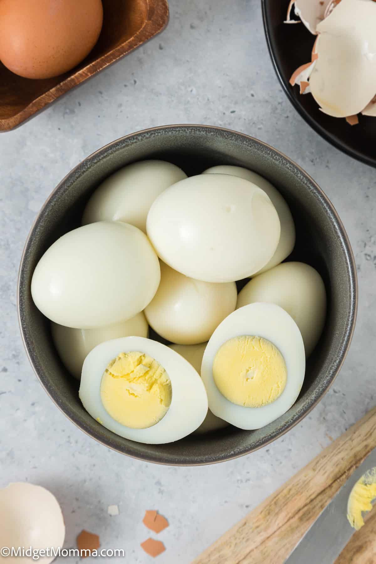 A bowl of hard-boiled eggs, some whole and one cut in half, showing the solid yellow yolk, placed on a light surface.