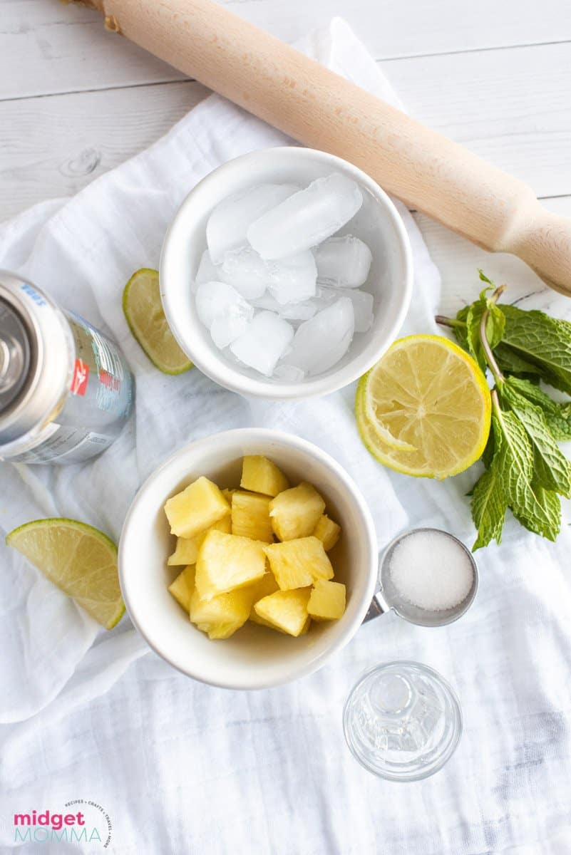 pineapple mojito ingredients -bowl with pineapple, bowl with ice, mint leave, lemon, lime and rum