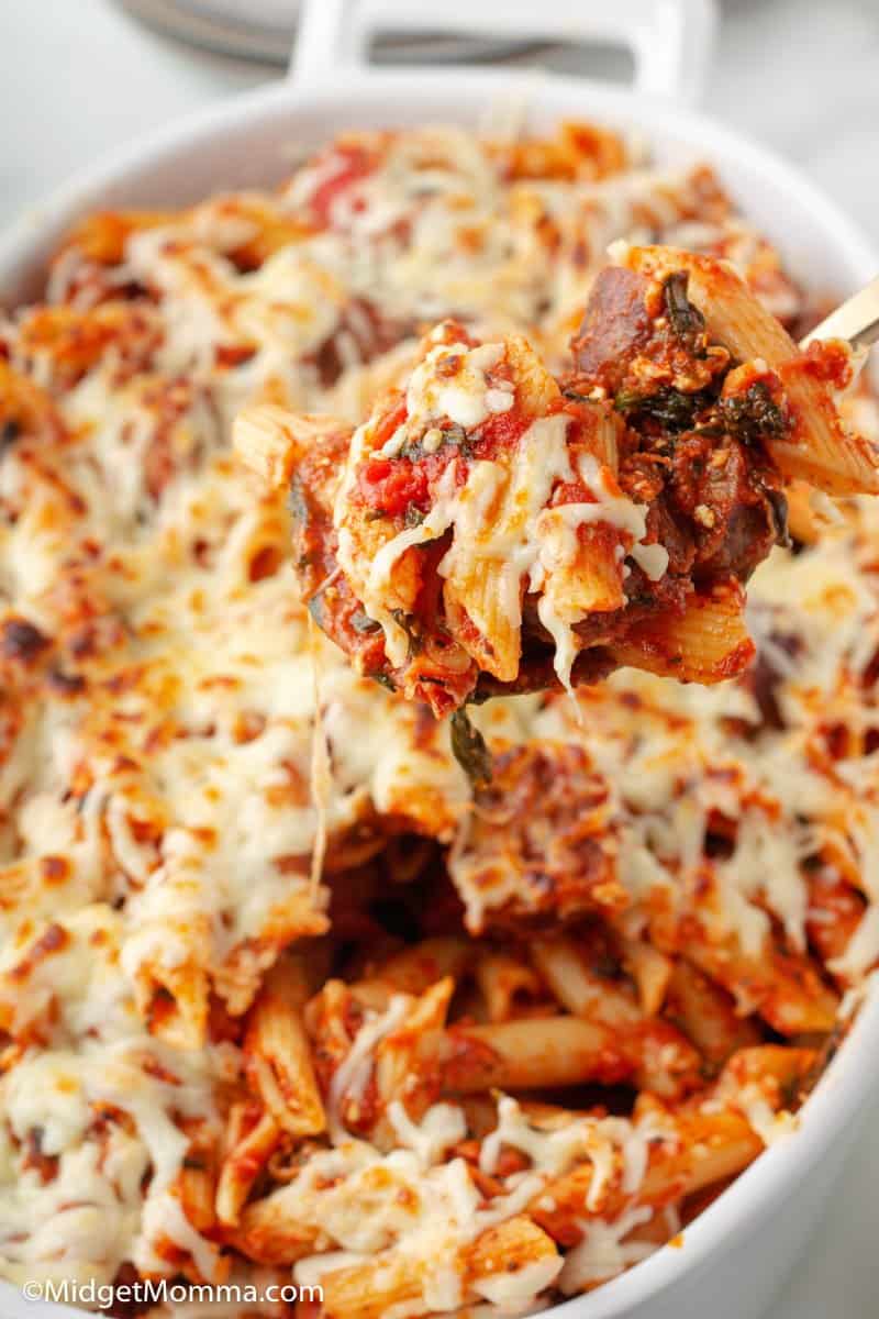 baked penne pasta being schooped with a spoon out of the dish