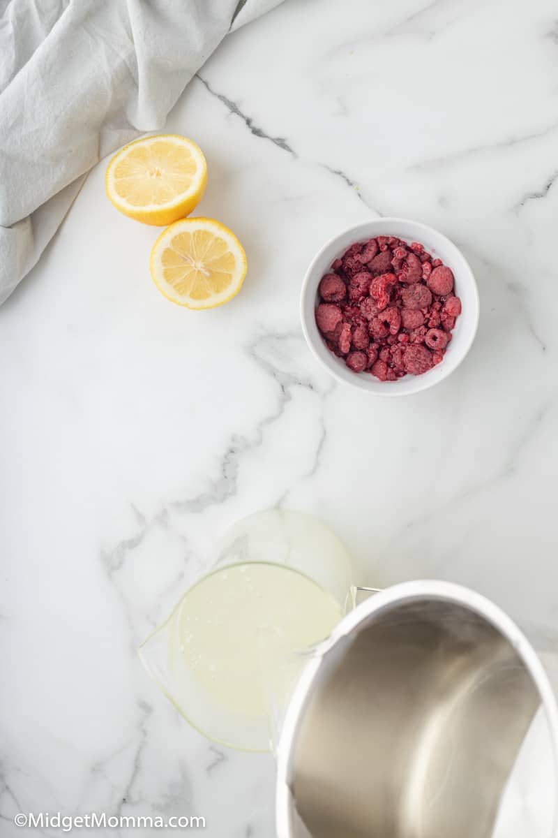 simple syrup being poured into water  and lemon juice to make raspberry lemonade