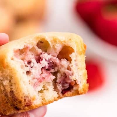 hand holding a strawberry muffin with a bite taken out