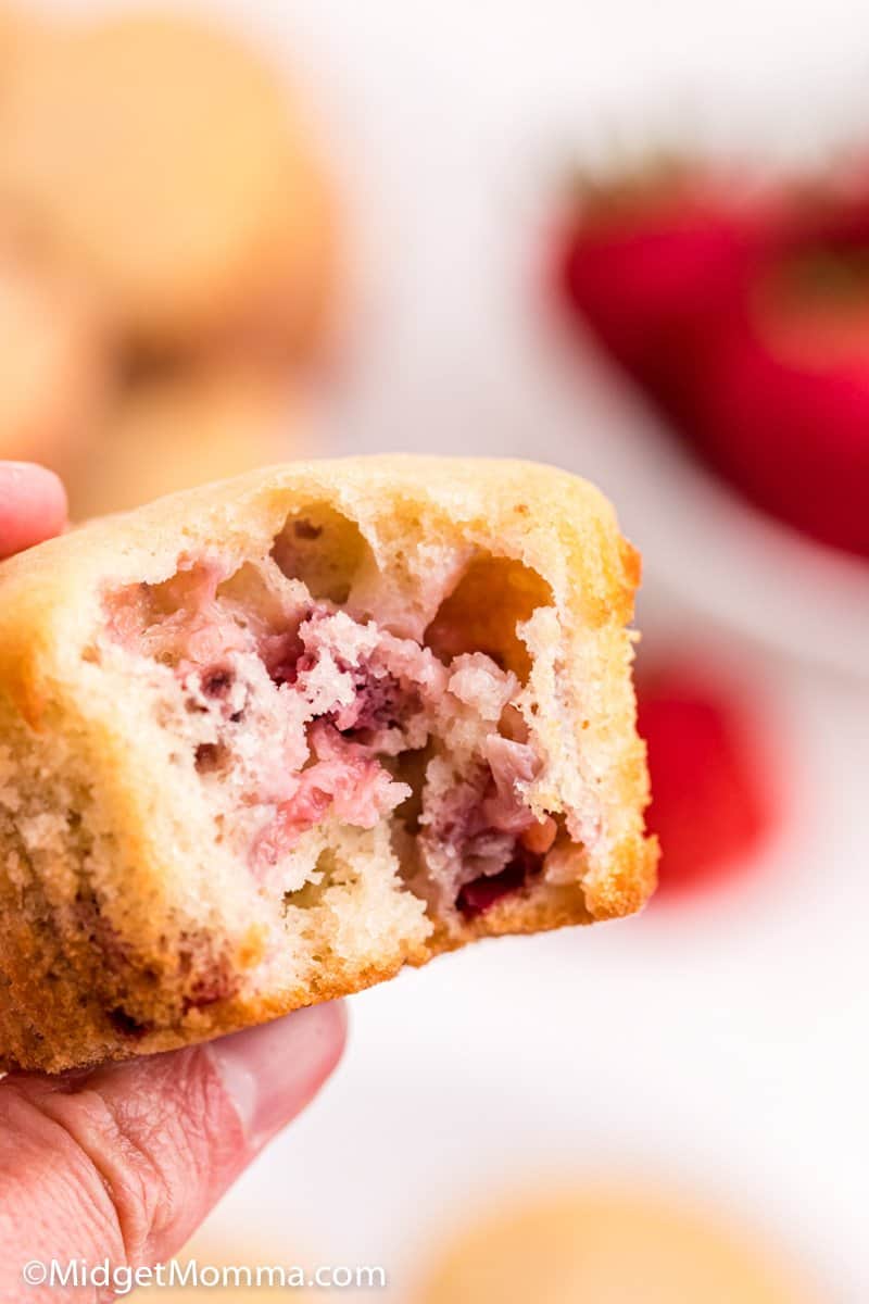 hand holding a strawberry muffin with a bite taken out