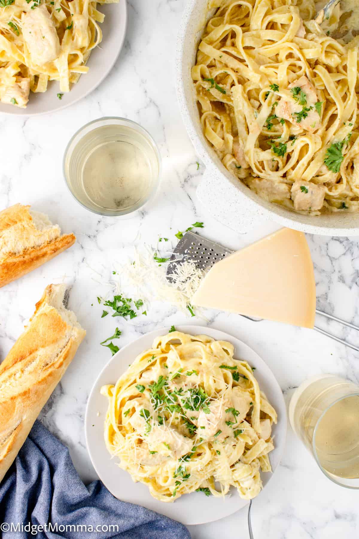 overhead photo of a plate of chicken alfredo pasta, with the serving dishe behind it and a loaf of bread