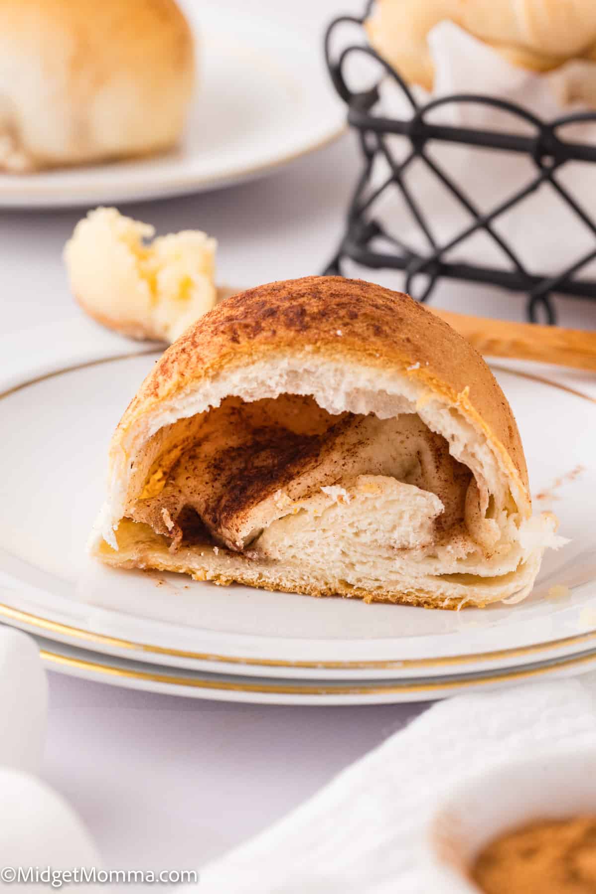 A cinnamon-filled bread roll is cut open on a white plate, showing a soft interior.