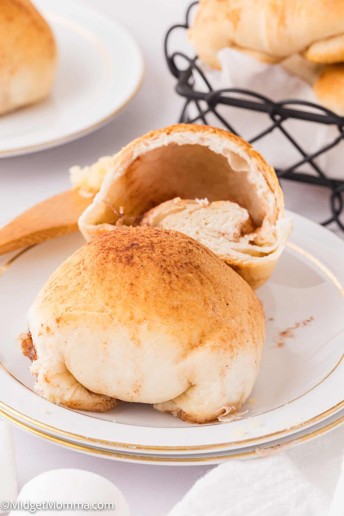 Two cinnamon rolls on a white plate; one is partially cut open. There's a glimpse of a serving basket in the background.