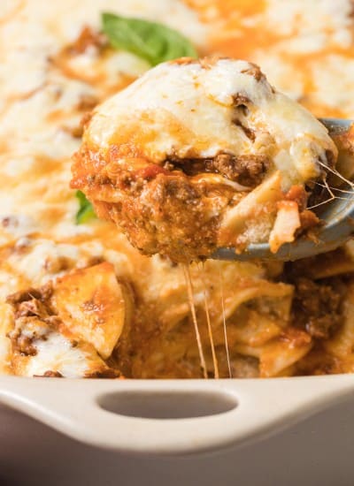 large serving spoon scoping Easy Baked Ravioli Casserole out of the baking dish.