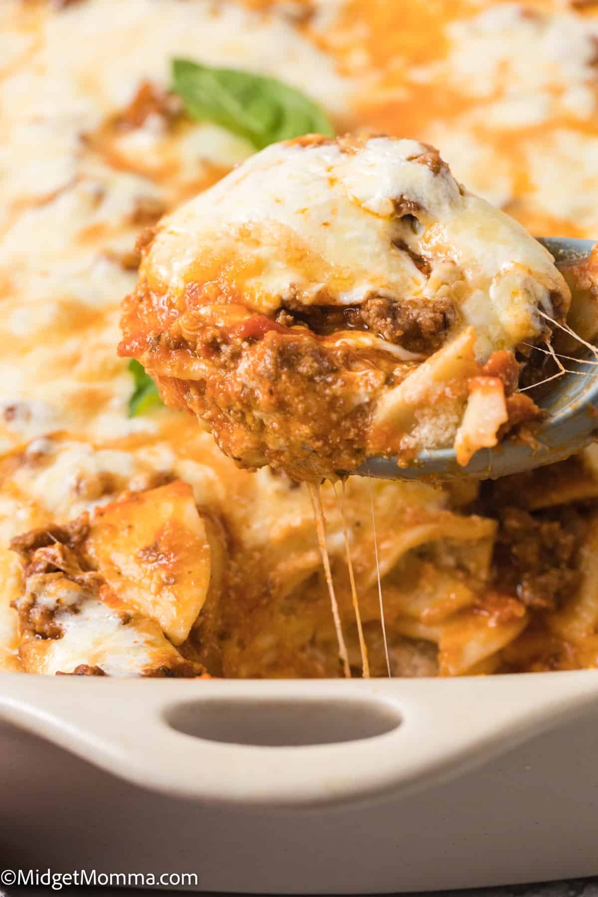 large serving spoon scoping Easy Baked Ravioli Casserole out of the baking dish.