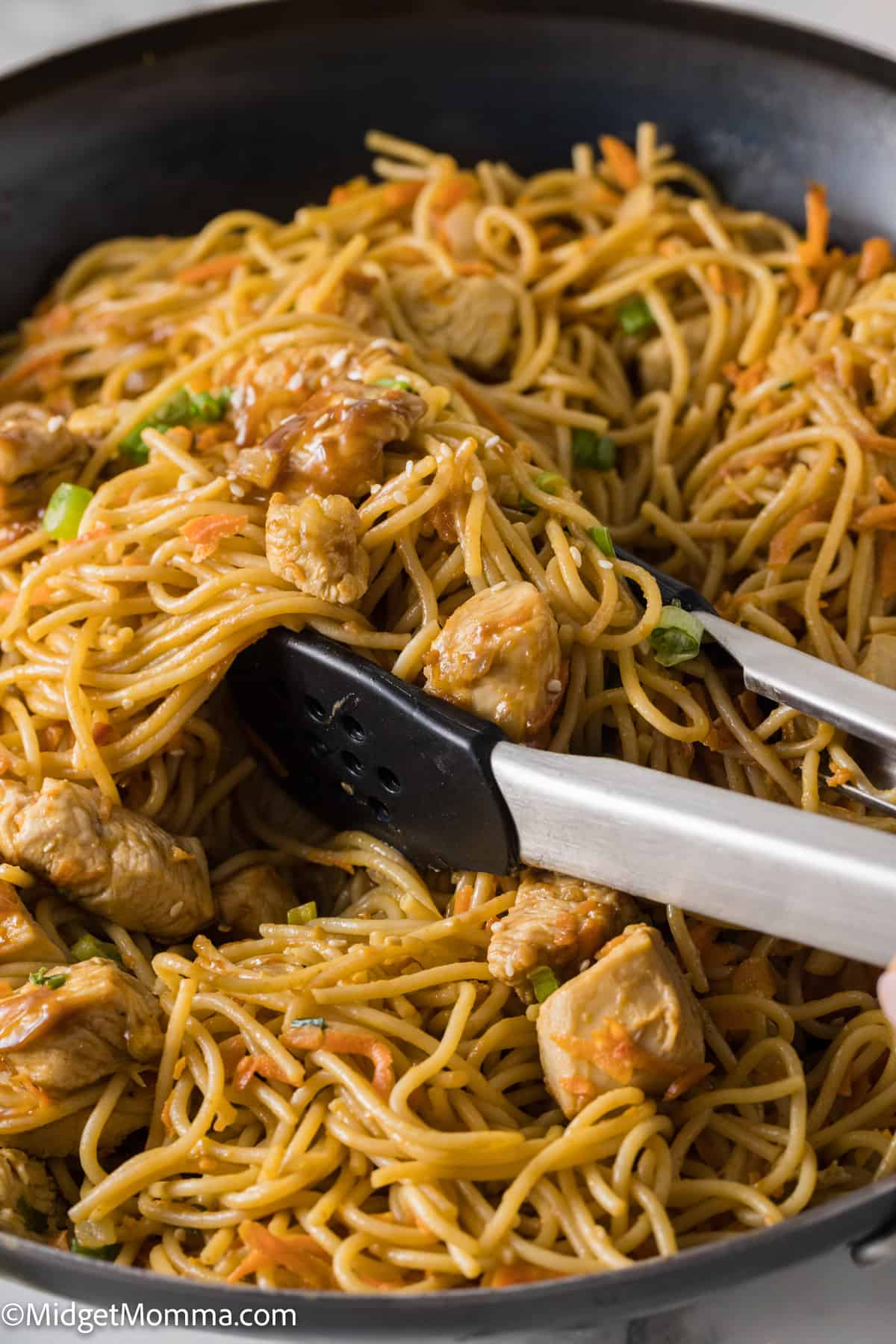 tongs serving Thai Peanut Noodles with Chicken from the skillet
