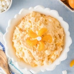 overhead photo of a white bowl filled with fluffy orange fluff salad topped with mandarin orange slices