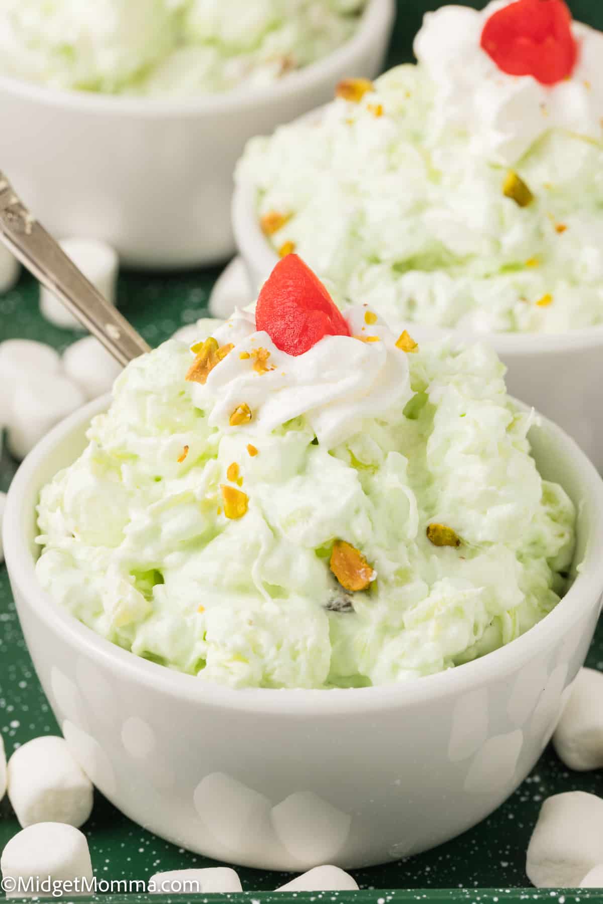 bowl of pistachio pudding salad being served topped with a cherry and chopped pecans