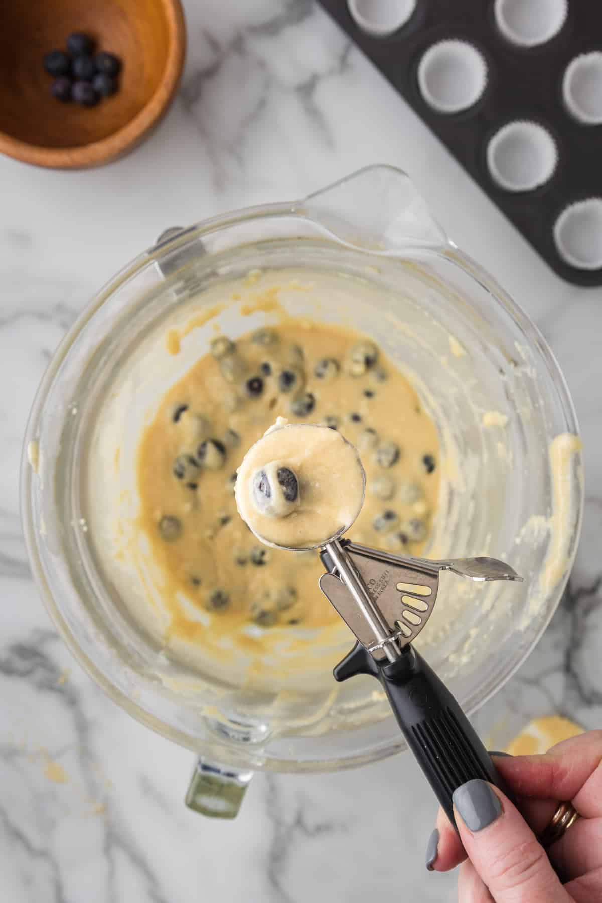 A person mixing blueberry muffin batter in a bowl.