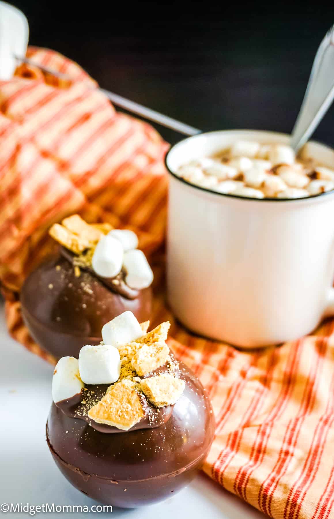 2 smores hot chocolate bombs and a cup of hot chocolate made with a hot chocolate bomb