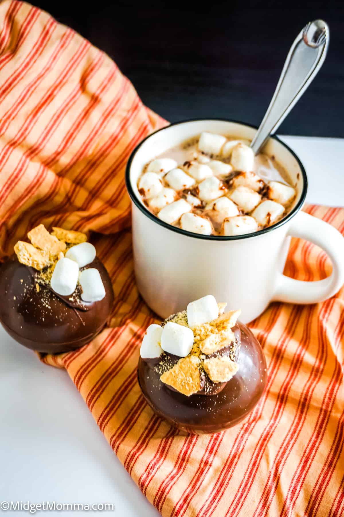 smores hot chocolate bombs next to a cup of hot chocolate made with a s'mores hot chocolate bomb