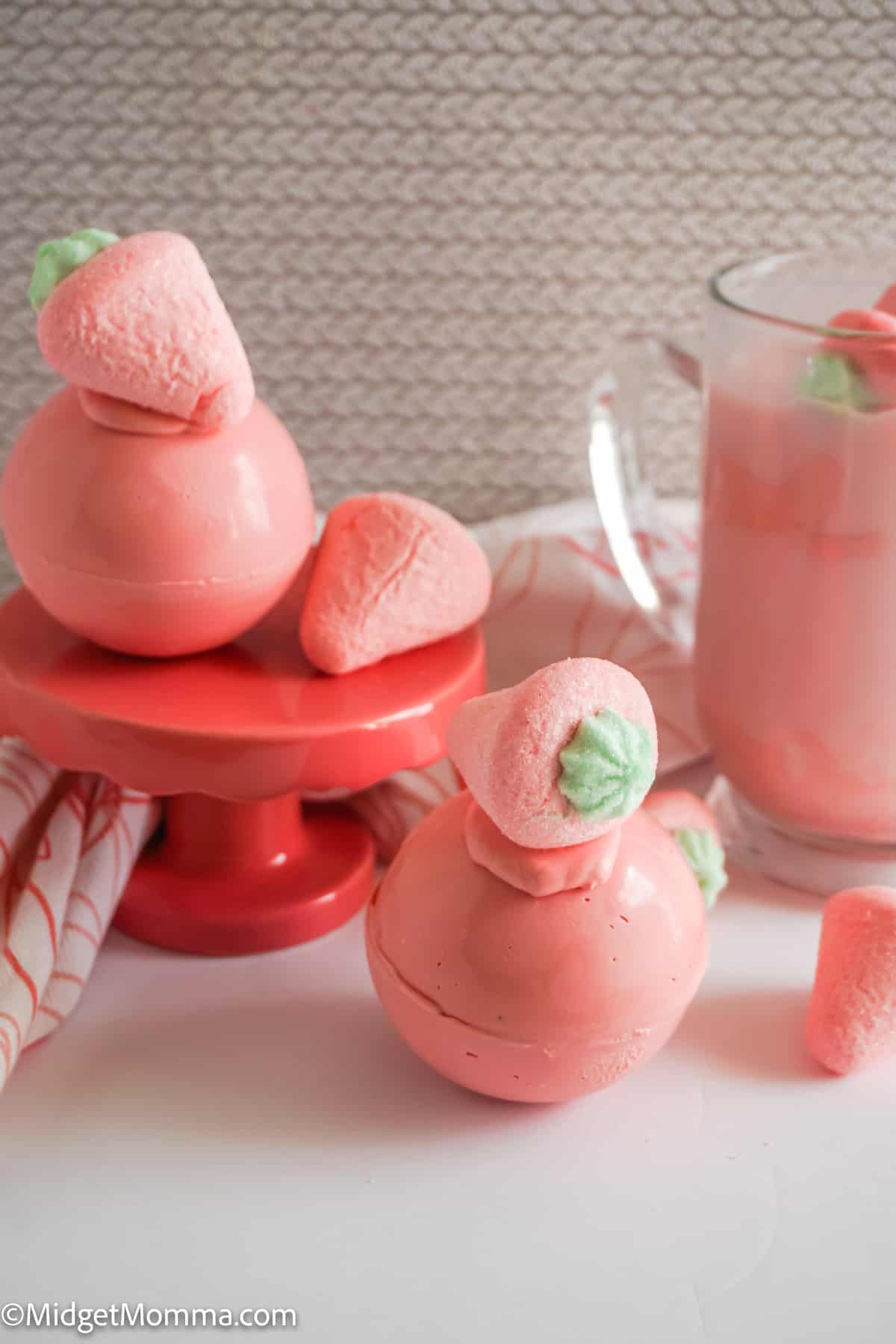 2 strawberry hot chocolate bombs next to a cup of strawberry hot chocolate 