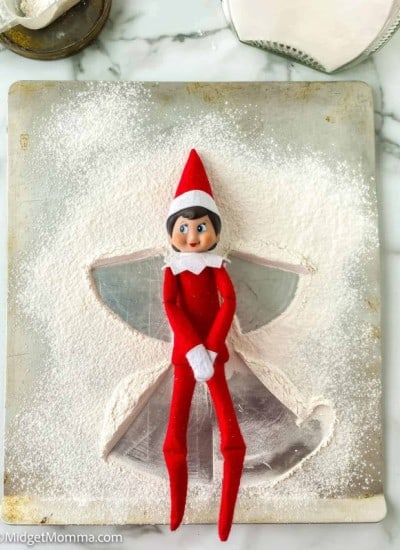 An elf on the shelf is sitting on top of a cookie sheet.