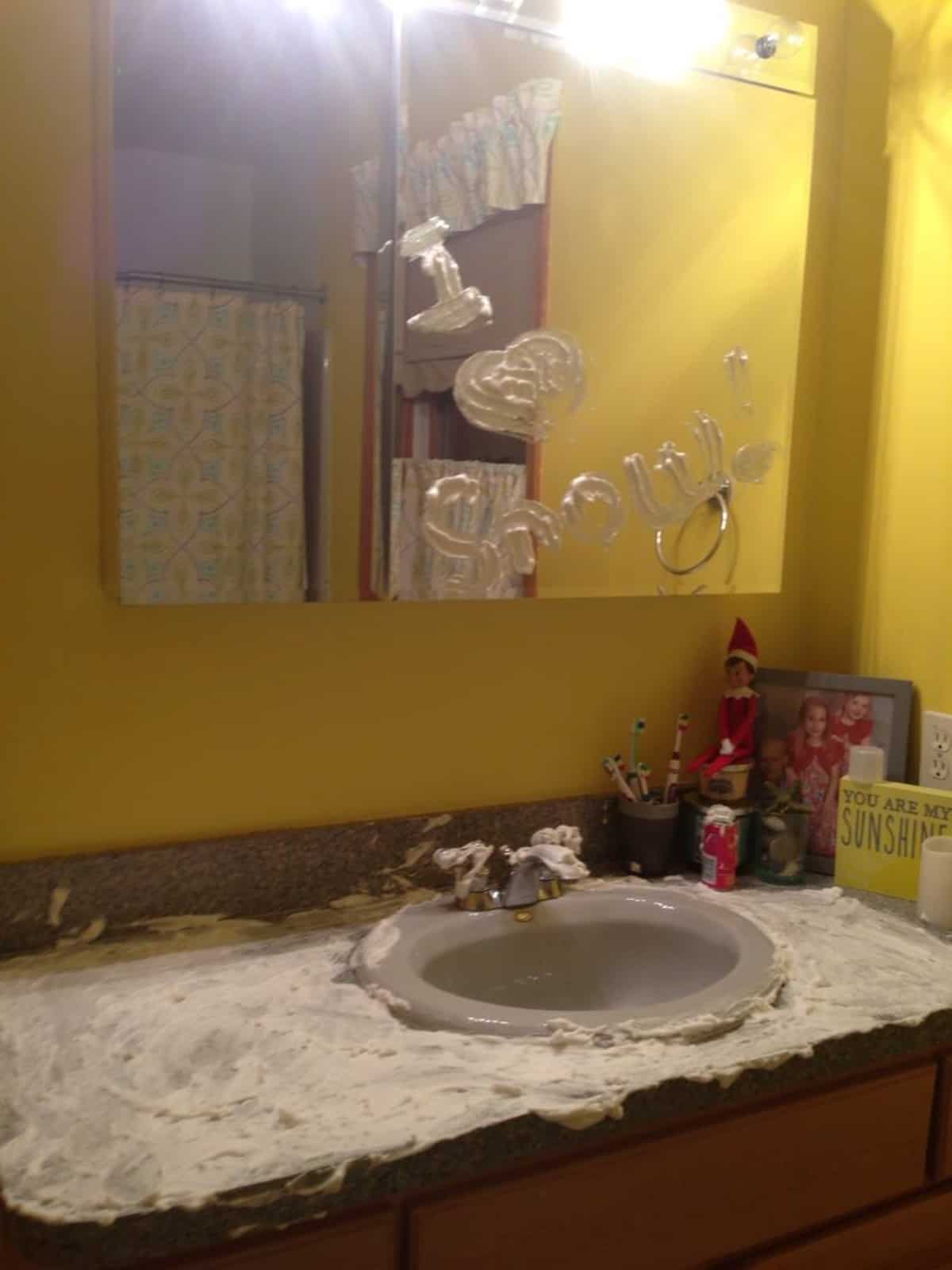 A yellow bathroom with a sink and mirror covered in a mess made by the elf