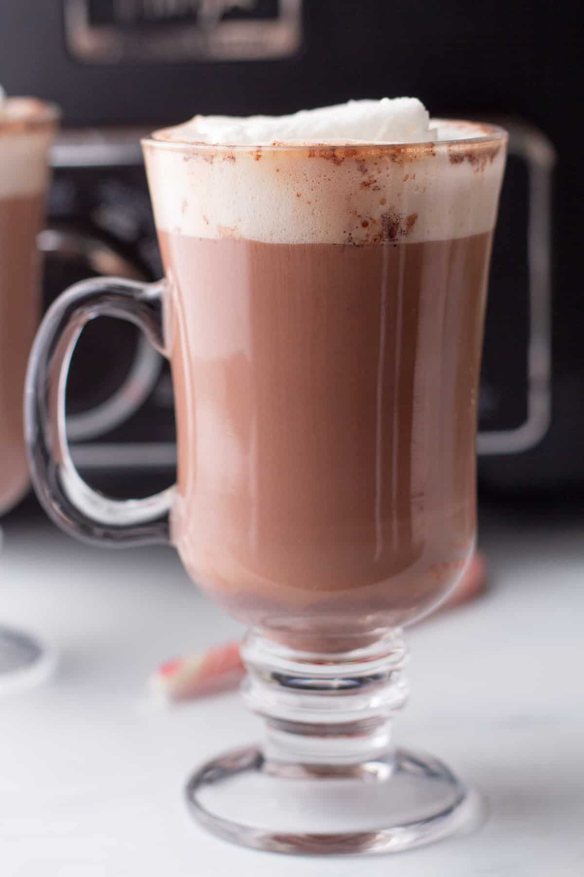 Two glasses of hot chocolate in front of a coffee maker.