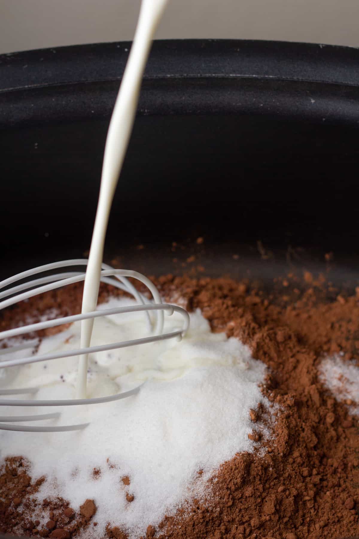 Whisking milk into a crockpot of hot cocoa ingredients including cocoa powder and sugar.