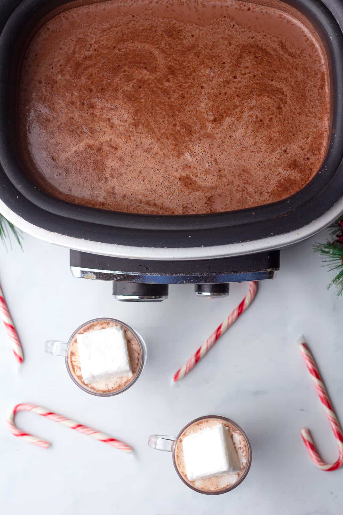 A crock pot filled with hot chocolate and candy canes.