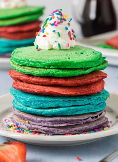 close up photo of a stack of rainbow pancakes - 2 green pancakes, 2 red pancakes, 2 blue pancakes, 2 purple pancakes